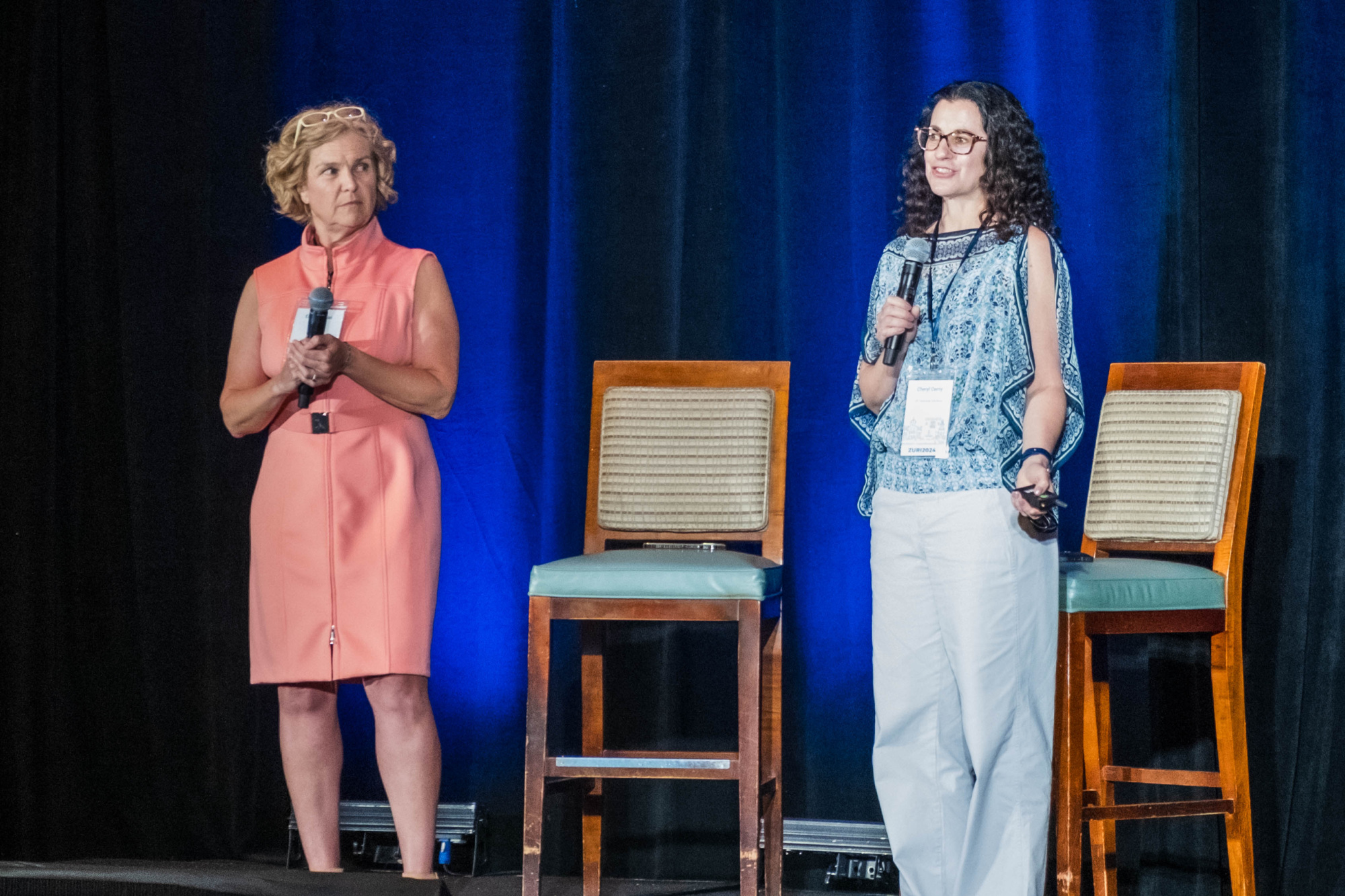 Two women standing on a stage speaking to a crowd at a conference